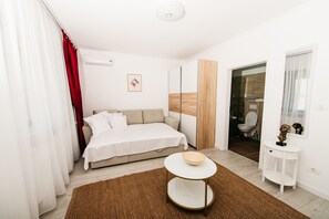 A modern bedroom with a bed, a round table, a small white side table, and a bathroom visible through an open door.