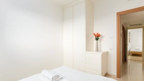 Ein Hotelzimmer mit einem Bett, einem Schminktisch mit Blumen in einer Vase und einer Holztür, die in einen anderen Raum führt.