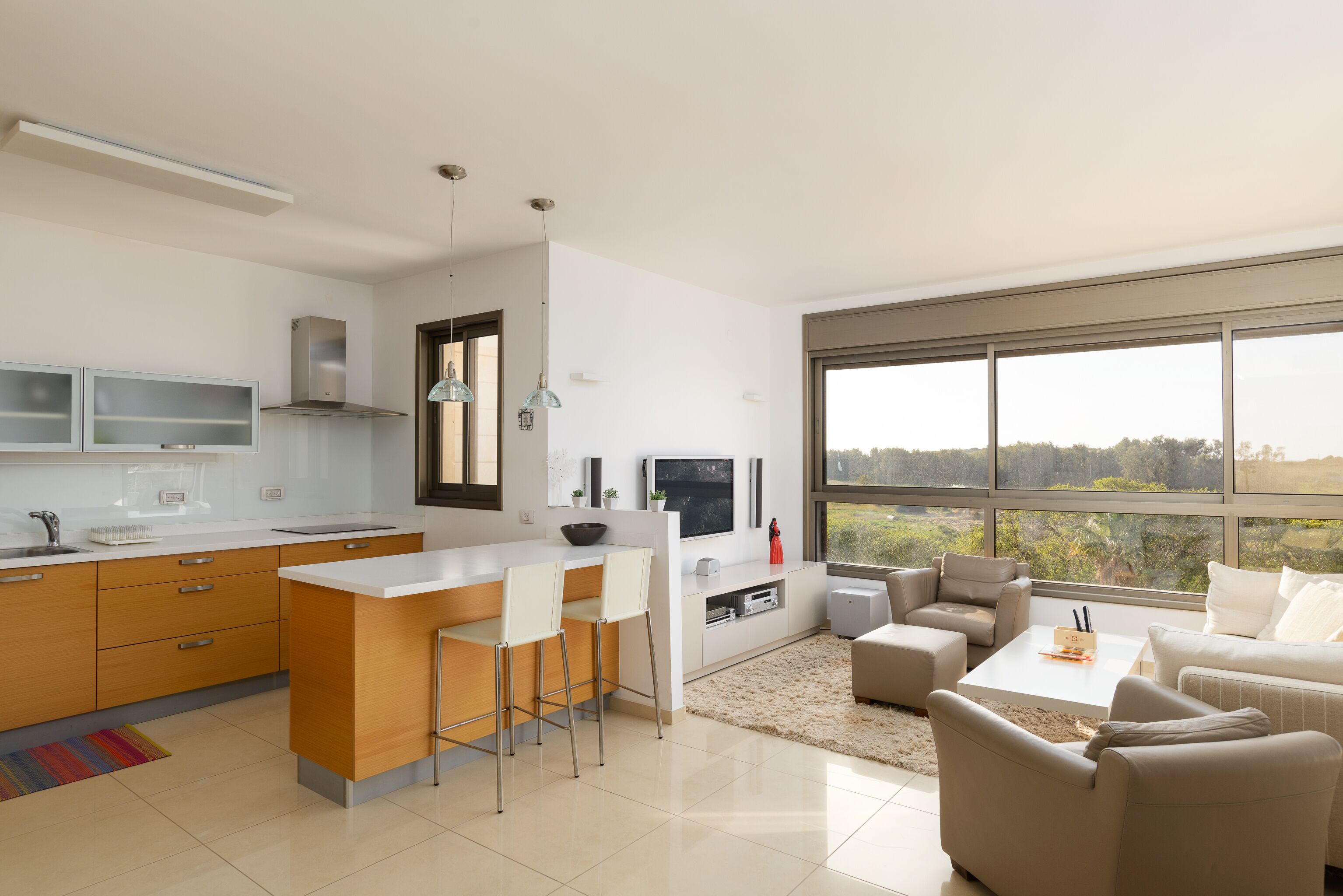 A modern kitchen with a central island, bar stools, and a dining area with a sofa and coffee table.
