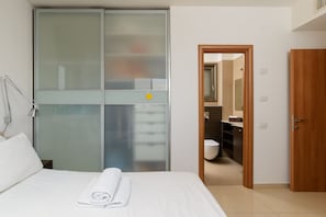 A hotel room with a bed, a bedside lamp, a wardrobe, and a bathroom visible through an open door. - Comfort with Terrace over the Hills by FeelHome (Tel Aviv)