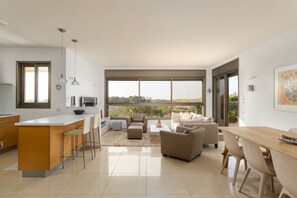 A modern kitchen with a central island, bar stools, and a dining area with a wooden table and chairs. - Comfort with Terrace over the Hills by FeelHome (Tel Aviv)