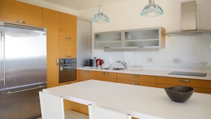 Eine moderne Küche mit einem Edelstahl-Kühlschrank, Holzschränken, einer weißen Arbeitsplatte und zwei Pendelleuchten.