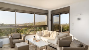 Ein modernes Wohnzimmer mit Sofa, Sesseln, einem Couchtisch und großen Fenstern mit Blick auf die Landschaft.