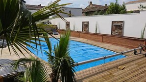 En swimmingpool med en træterrasse, omgivet af en hvid mur med stenudsmykning og et tag med fliser.