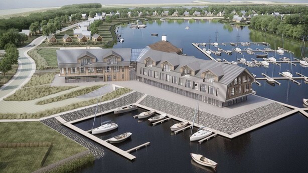 Un puerto deportivo con barcos amarrados, un edificio grande con techo inclinado y un paisaje circundante con árboles y senderos.