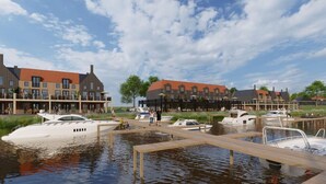 Una propiedad frente al agua con varios barcos amarrados, un muelle de madera y edificios de estilo europeo tradicional con tejados rojos.
