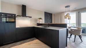 Una cocina moderna con armarios oscuros, una isla central, horno empotrado y una lámpara colgante.