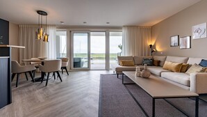 Una sala de estar moderna con sofá, mesa de centro y sillas. Tiene un balcón con vistas al exterior.