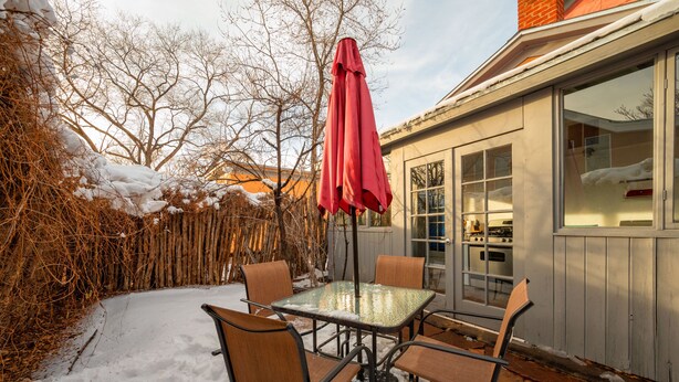 A patio with a glass table and chairs, a red umbrella, and a wooden fence. - Contemporary Style with Old World Charm (Santa Fe)