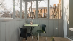 A corner room with a small table and two chairs, a window with a view of bare trees and a building, and wooden paneling on the walls. - Contemporary Style with Old World Charm (Santa Fe)