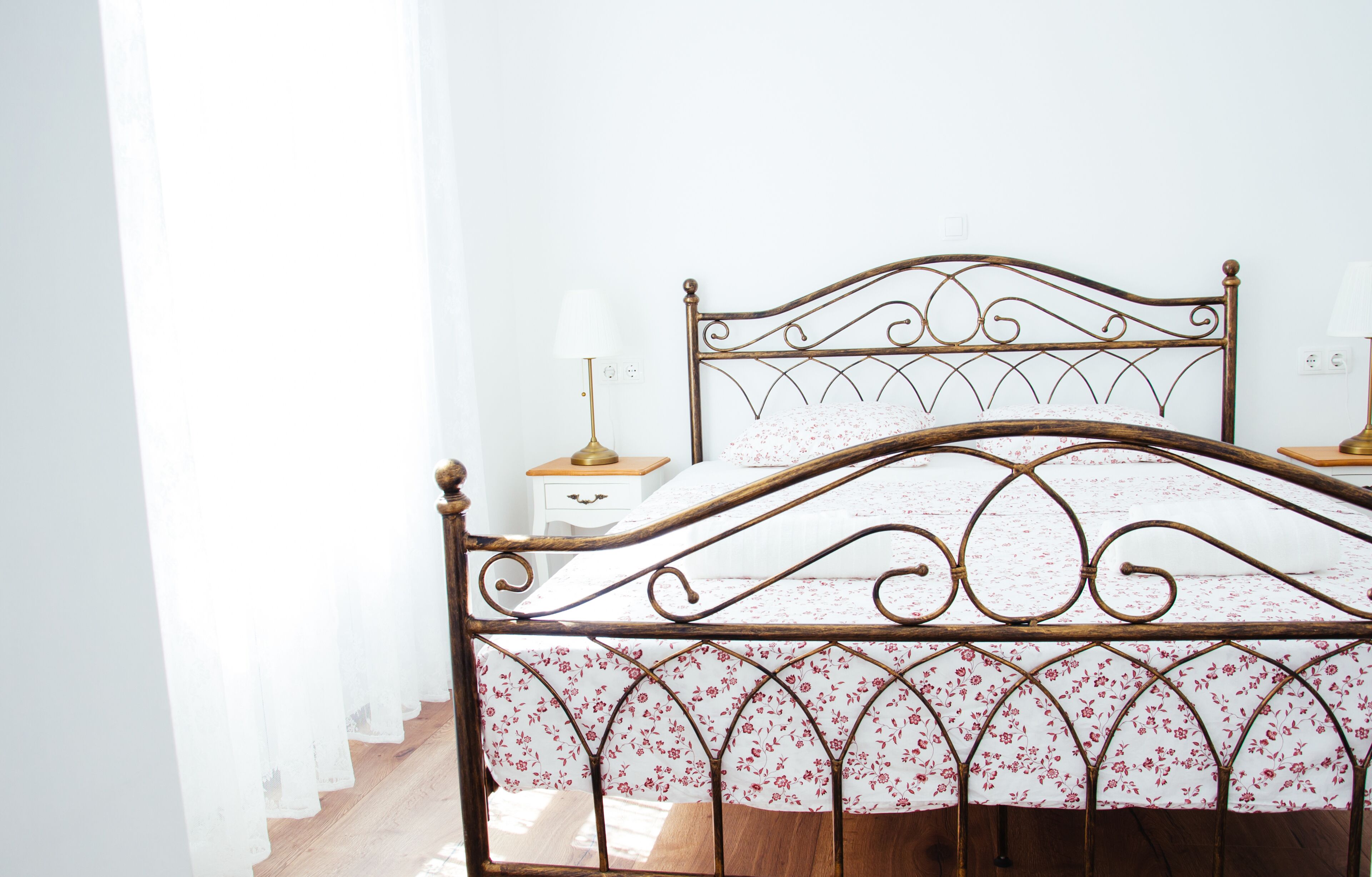 A bed with a metal frame and floral bedding, a bedside table with a lamp, and a white wall with a power outlet.