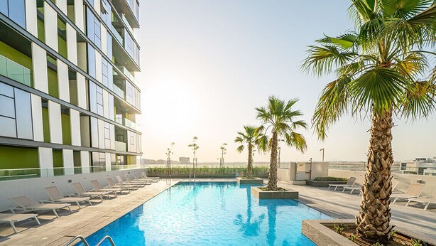 A modern hotel with a rooftop pool, lounge chairs, and palm trees. - Nasma Luxury Stays - Pulse Residence  (Dubai)