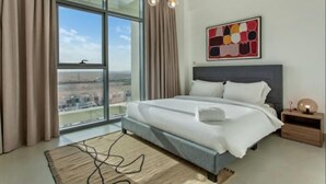 A modern bedroom with a large bed, a view of the city, and a contemporary art piece on the wall. - Nasma Luxury Stays - Pulse Residence  (Dubai)
