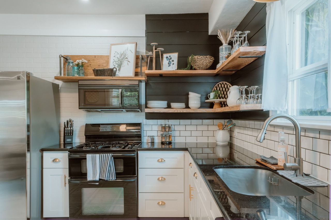Cocina compacta con microondas integrado, estufa y lavamanos. Hay repisas de madera sobre la encimera que sostienen distintos utensilios de cocina.