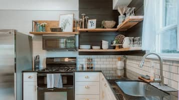 A compact kitchen with a built-in microwave, stove, and sink. There are wooden shelves above the counter holding various kitchen items.