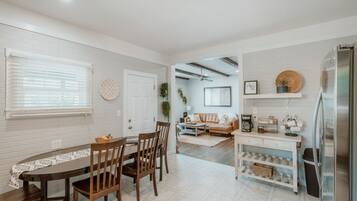 Una cocina moderna con paredes de ladrillo blanco, un comedor con mobiliario de madera y un espacio de sala con sofá y mesa de centro.