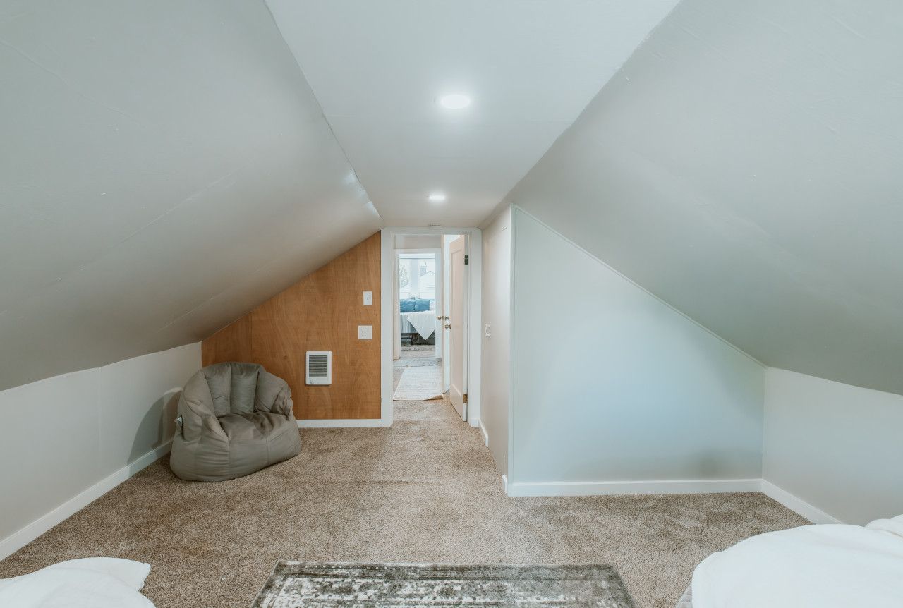 Una habitación estrecha en el ático con techo inclinado, un sillón de peluche y suelo alfombrado.
