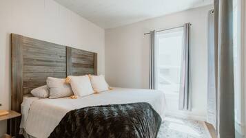 Un dormitorio con una cama grande, cabecera, mesita de noche y ventana con cortinas.