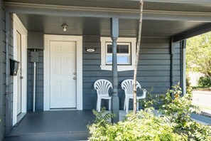 A house with a front door, a mailbox, and two white plastic chairs on the porch.