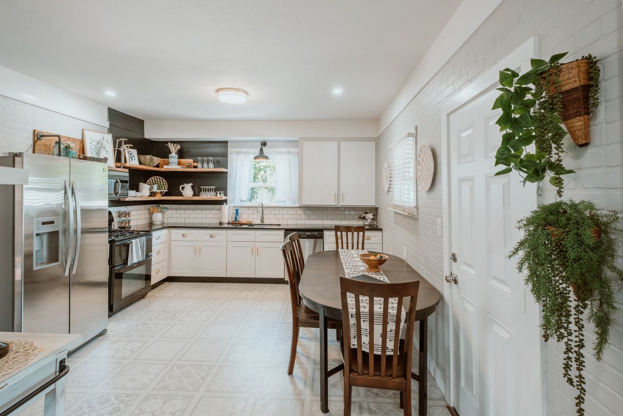 Una cocina moderna con muebles blancos, un refrigerador de acero inoxidable y una mesa de comedor con sillas.