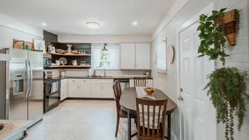 Una cocina moderna con muebles blancos, un refrigerador de acero inoxidable y una mesa de comedor con sillas.