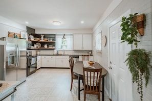 A modern kitchen with white cabinetry, a stainless steel refrigerator, and a dining table with chairs. - A beautiful home near OSU campus (Corvallis)