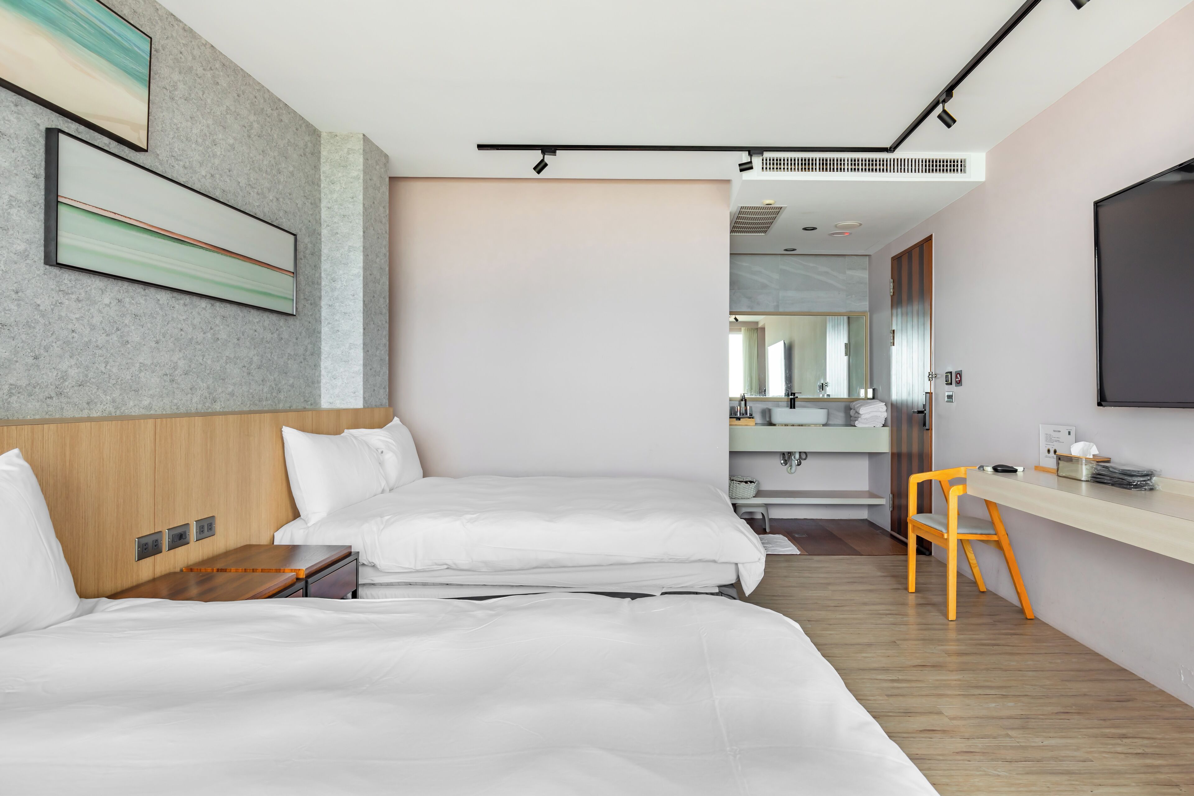 Et moderne hotelværelse med en stor seng, et skrivebord og en stol. Der er et spejl og et fjernsyn på væggen.