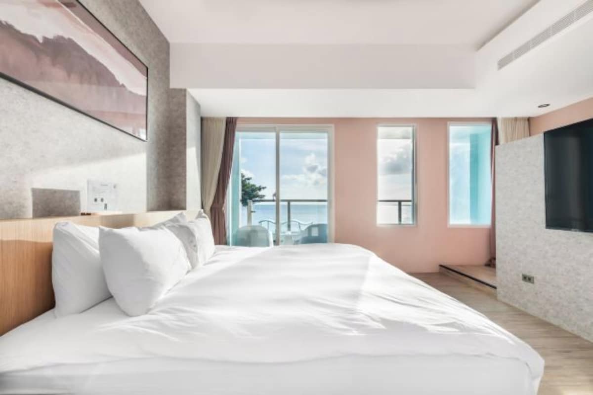 A modern hotel room with a large bed, a view of the sea, and a balcony.