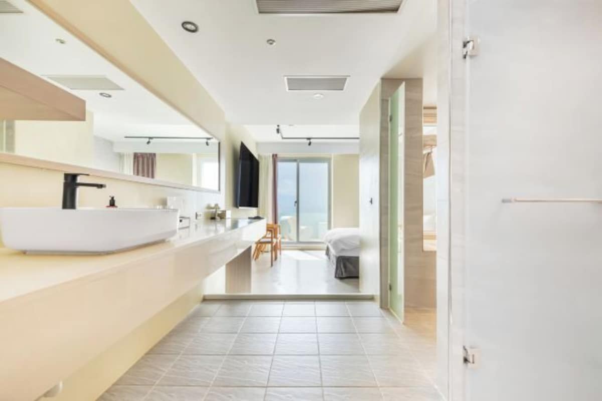 A modern bathroom with a large white sink, a mirror, and a view of a balcony.