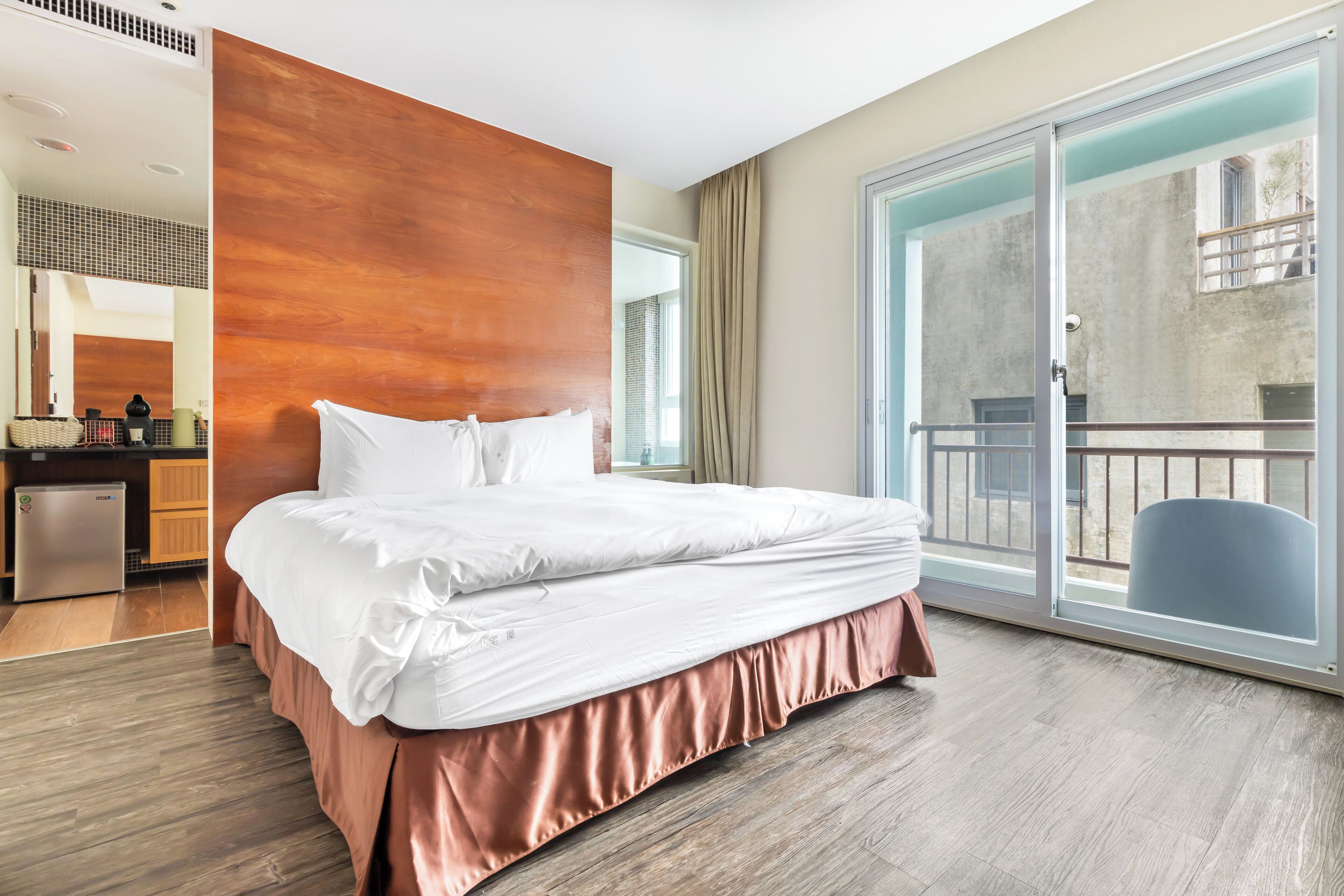Habitación de hotel con una cama grande, una puerta corrediza de vidrio a un balcón y una zona de kitchenette.