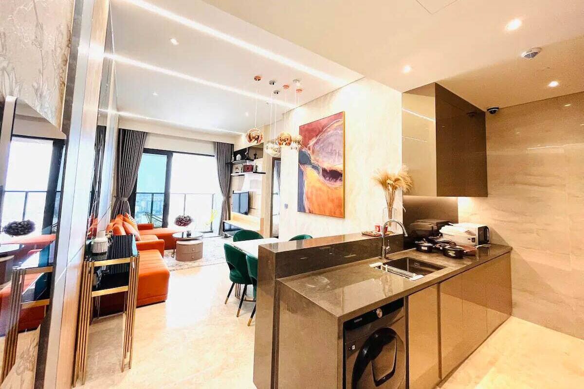 Une cuisine moderne dotée d’un îlot central, un coin repas avec une chaise verte et un espace de vie comprenant un canapé et une table.