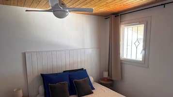 Een slaapkamer met een houten plafond, een bed met beddengoed met een patroon, een nachtkastje en een raam met gordijnen.