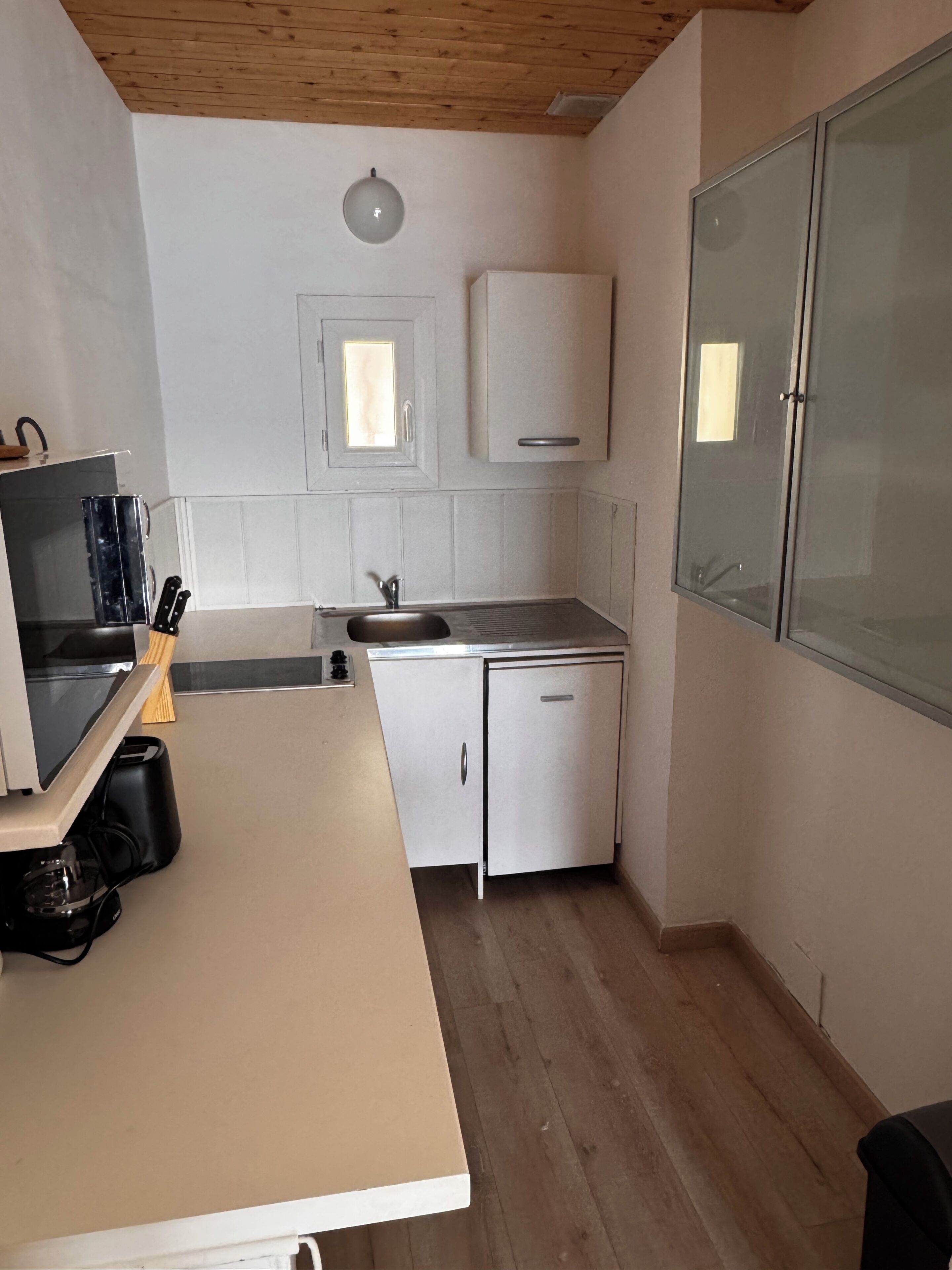 A compact kitchen with a wooden ceiling, a built-in sink, a small countertop, and a cabinet with a frosted glass door.