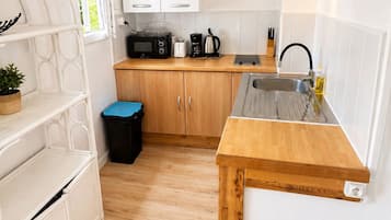 A compact kitchen with white cabinets, a microwave, a coffee maker, and a sink.