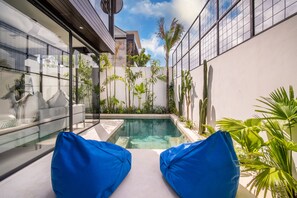 Un espace piscine extérieur moderne, doté de sièges rembourrés bleus et d’une végétation tropicale luxuriante.