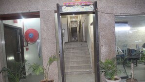 Entrada de un edificio con puerta de cristal, manguera contra incendios roja y plantas en macetas.