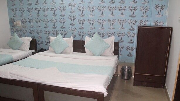 Habitación de hotel con dos camas, cada una con ropa blanca y almohadas azul claro, un armario de madera y un papel tapiz estampado.