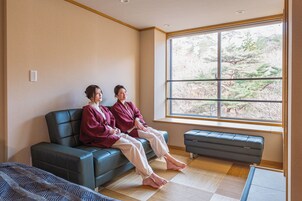 Quarto com sofá, um banco, uma janela grande com vista para árvores e uma mesa pequena.