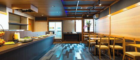 A modern restaurant interior with a long counter, wooden chairs, and a patterned floor.