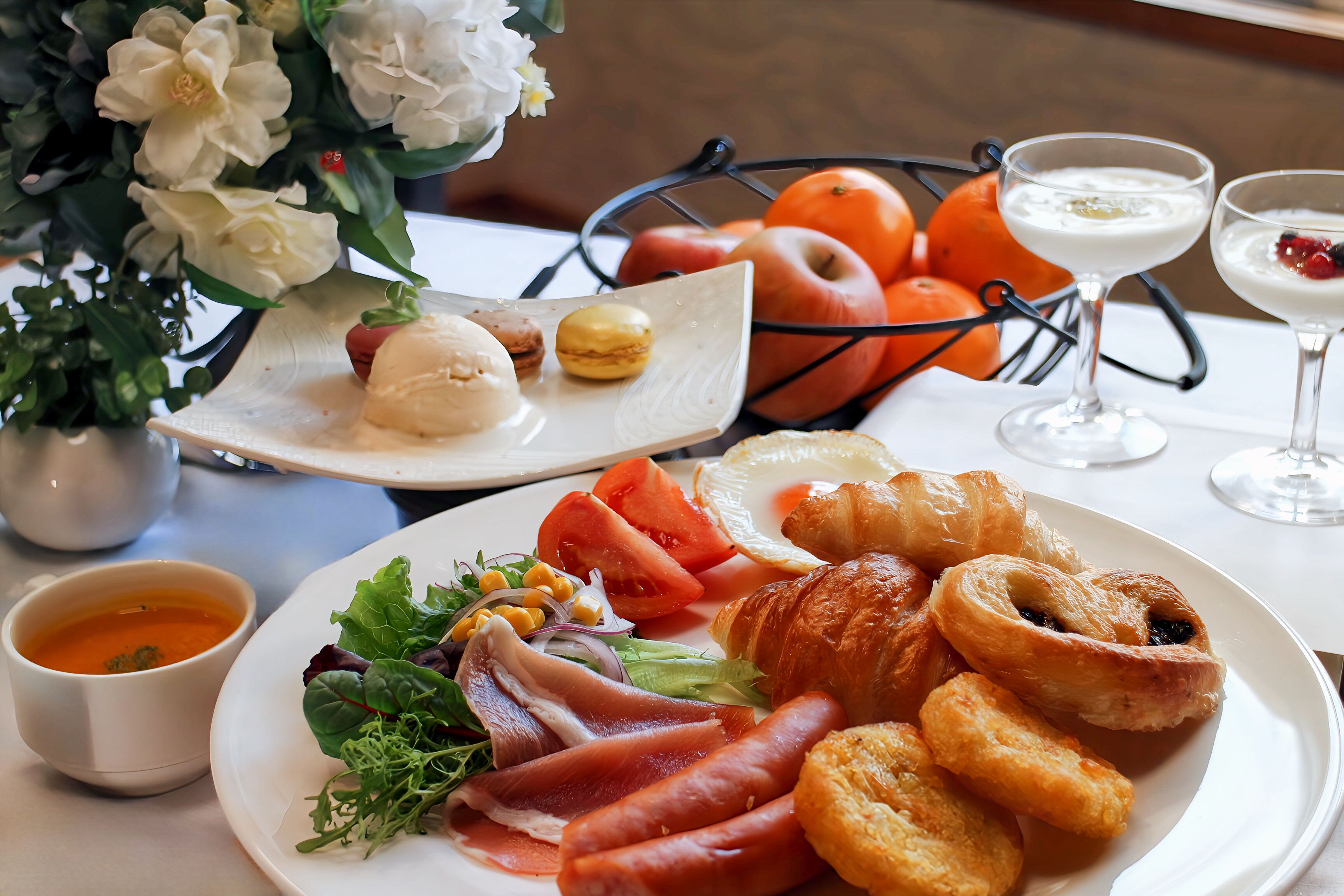 A breakfast plate with croissants, ham, tomatoes, and a salad.