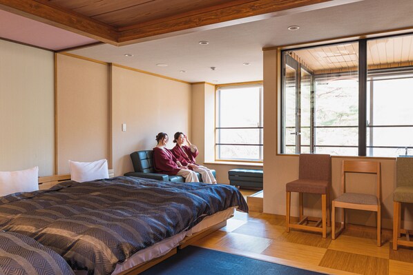 Un dormitorio con cama, dos sillas, escritorio y ventanas amplias.