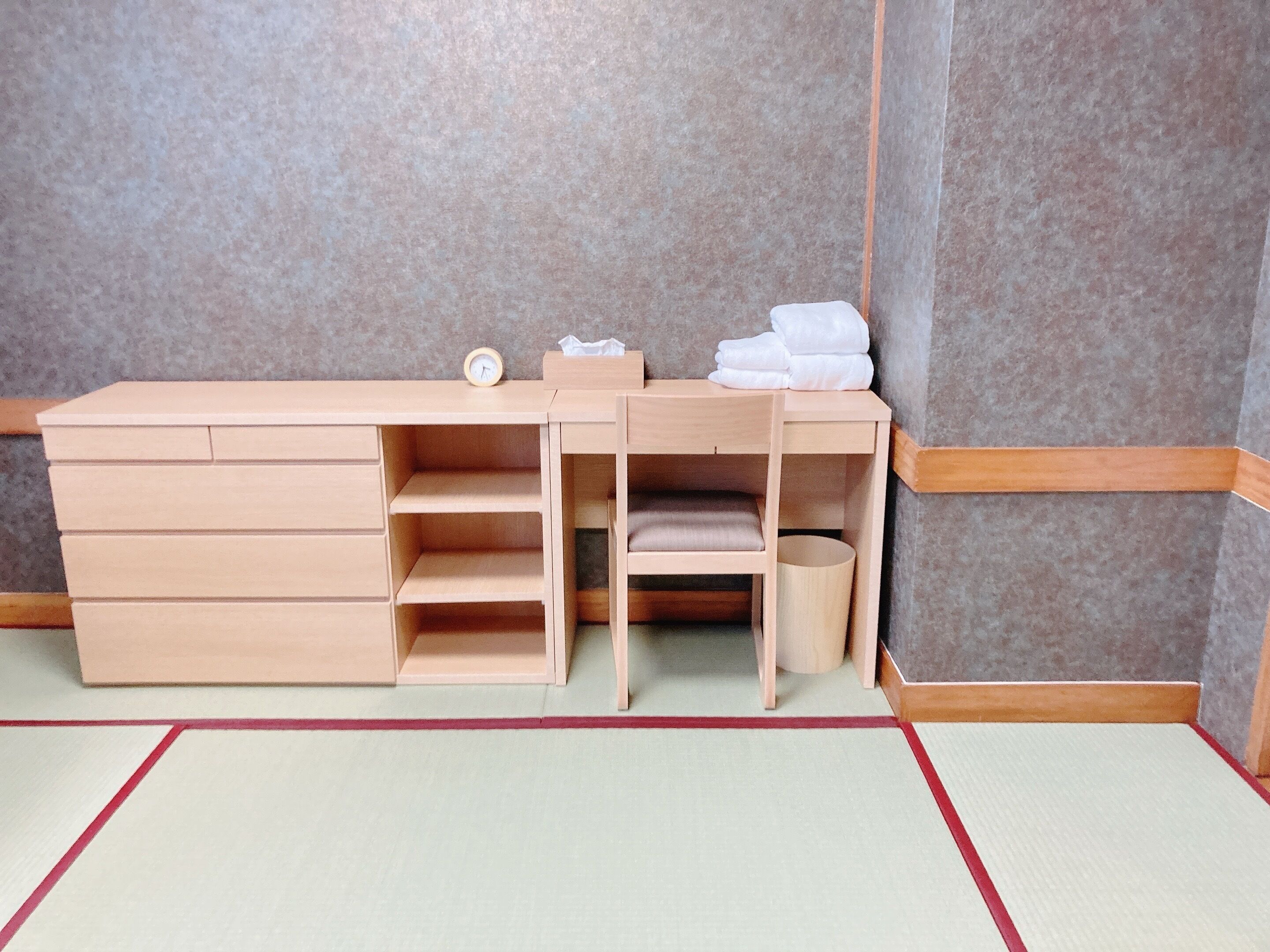 Un bureau en bois avec des tiroirs, une chaise, une petite étagère et une horloge.