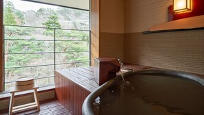 A traditional Japanese onsen with a wooden bench, a hot spring tub, and a view of a forested area through large windows. - Nikko Garden Hotel (Nasushiobara)