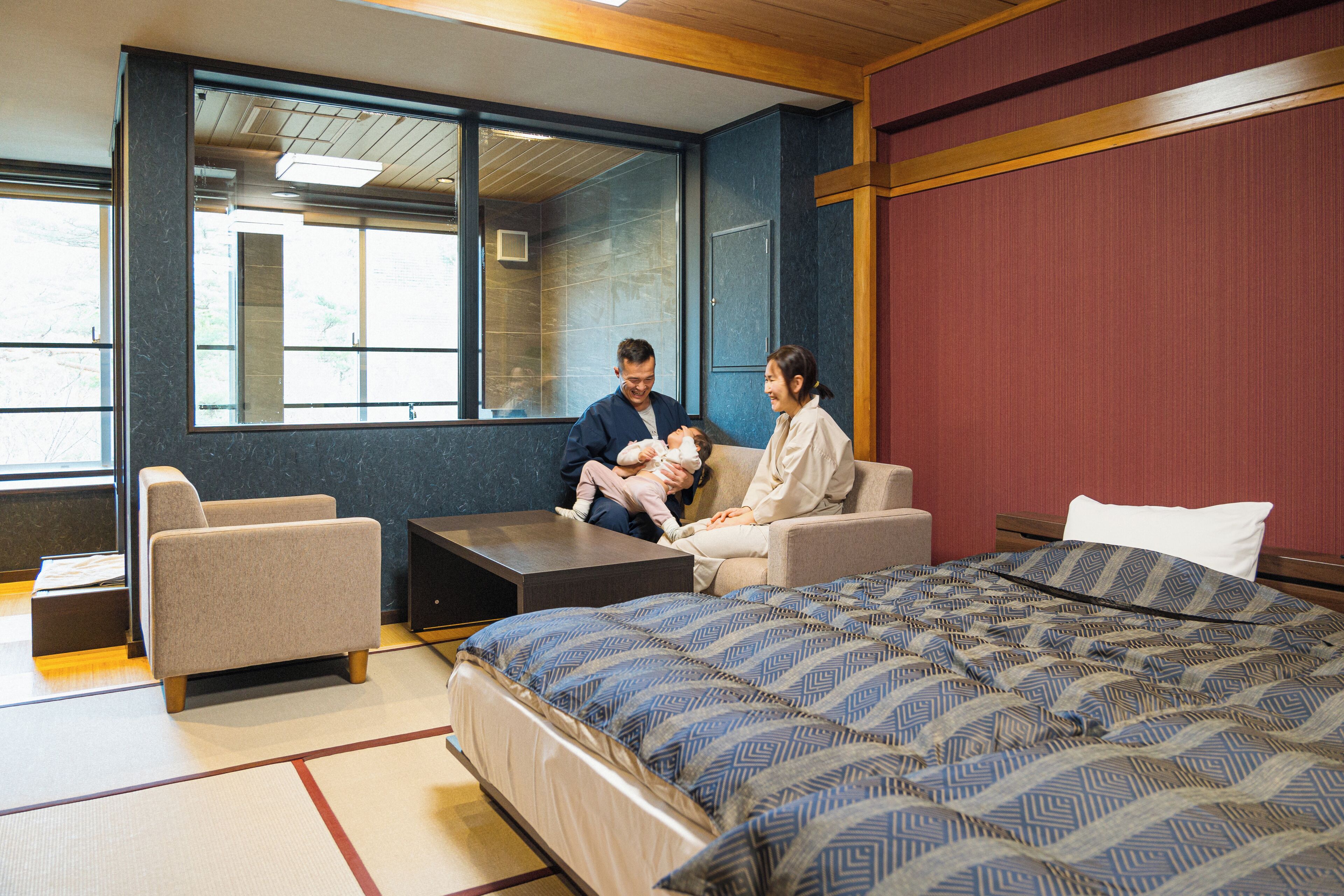 A hotel room with a bed, two chairs, a small table, and a large window.