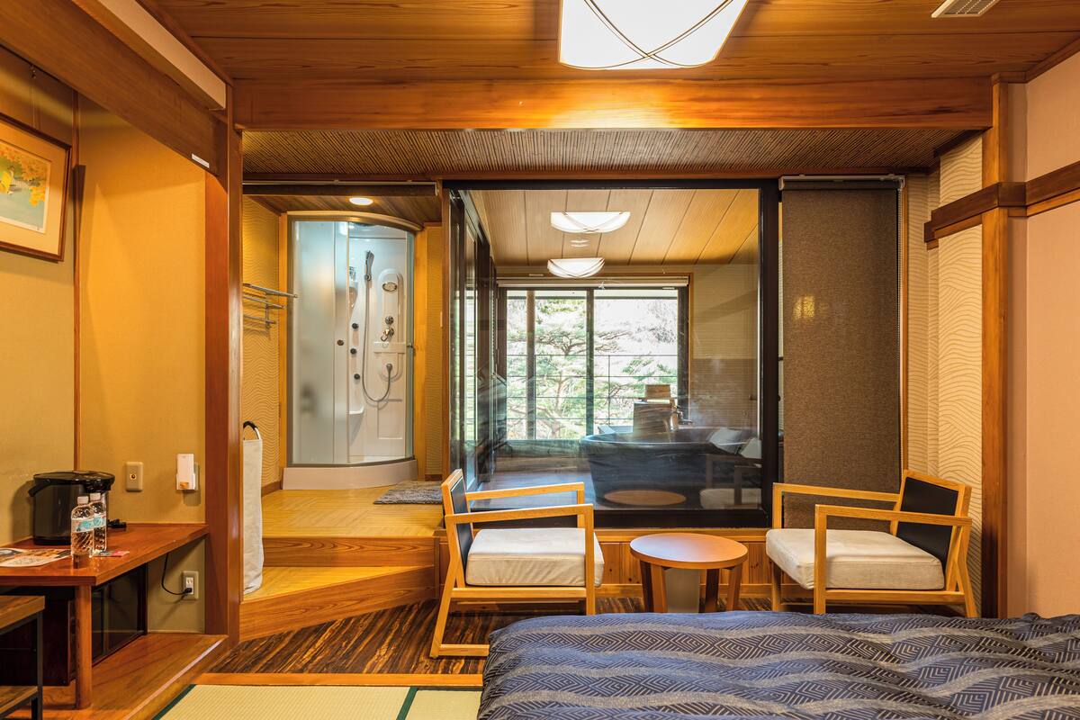 Habitación de hotel con cama, dos sillas, una mesita, un escritorio y vistas al exterior.