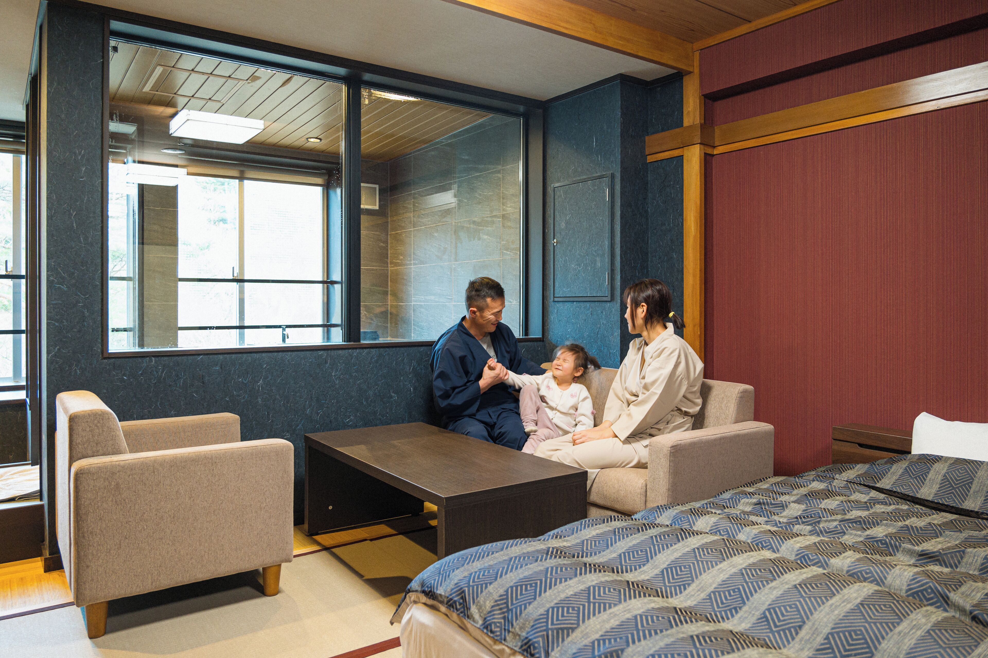 Ein Hotelzimmer mit großem Fenster, einem Bett mit gemustertem Überwurf, einer Couch und einem kleinen Tisch.