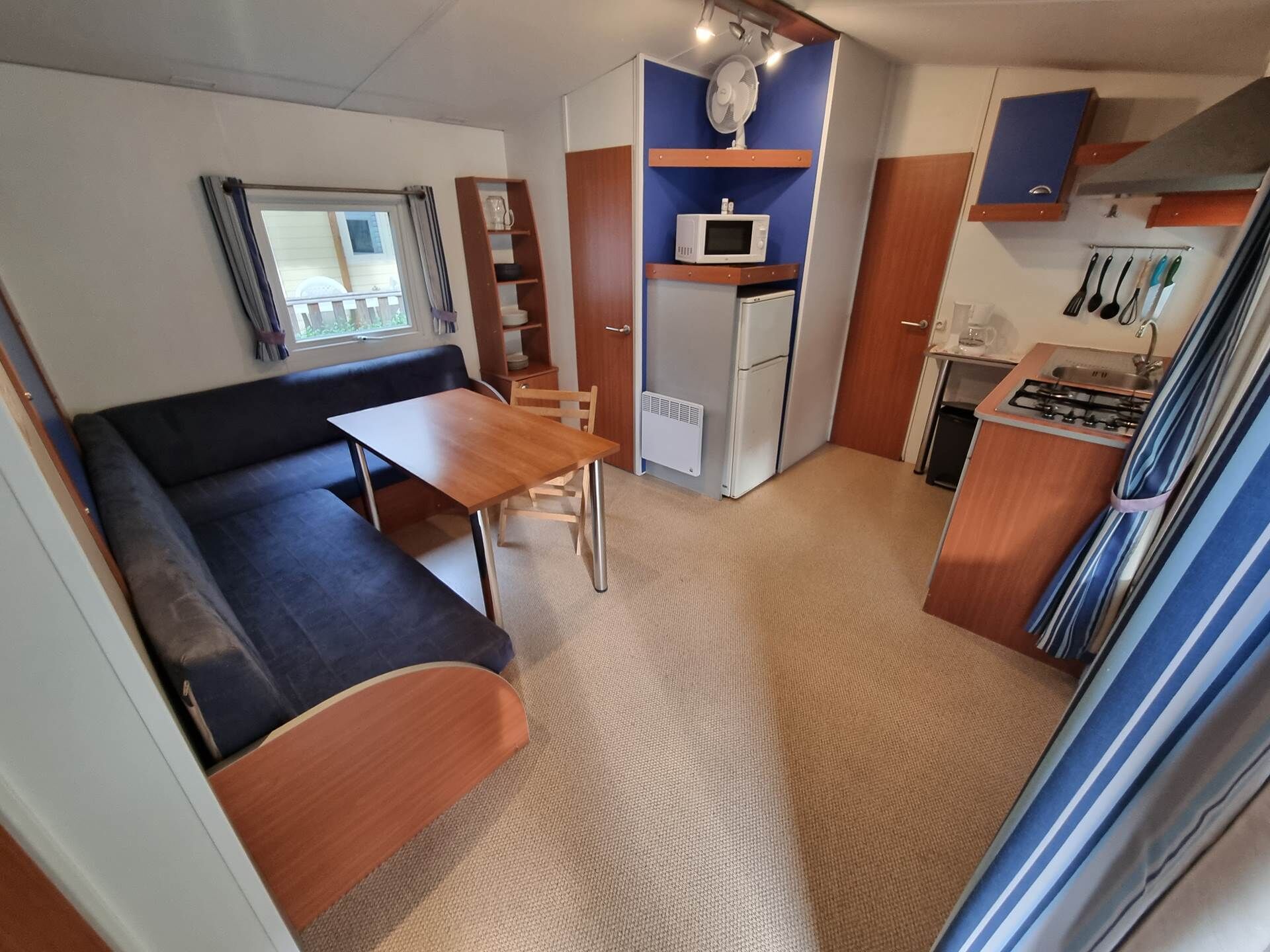 Una kitchenette compacta equipada con microondas, refrigerador y estufa a gas. Hay un pequeño comedor con mesa y sillas.