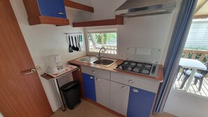 Une cuisine compacte équipée d’une cuisinière à gaz, d’un évier et d’une fenêtre donnant sur une terrasse.
