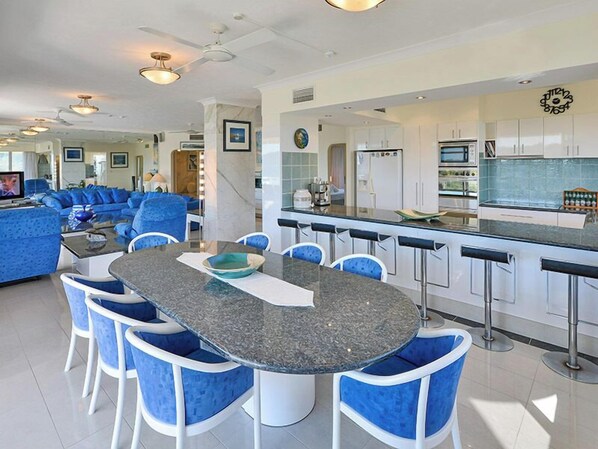 A modern kitchen with white cabinets, a central island with bar stools, and a dining area with blue chairs.
