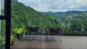A balcony with two hexagonal chairs and potted plants, overlooking a mountainous landscape with a village below. - Warm Place (Zhangjiajie)